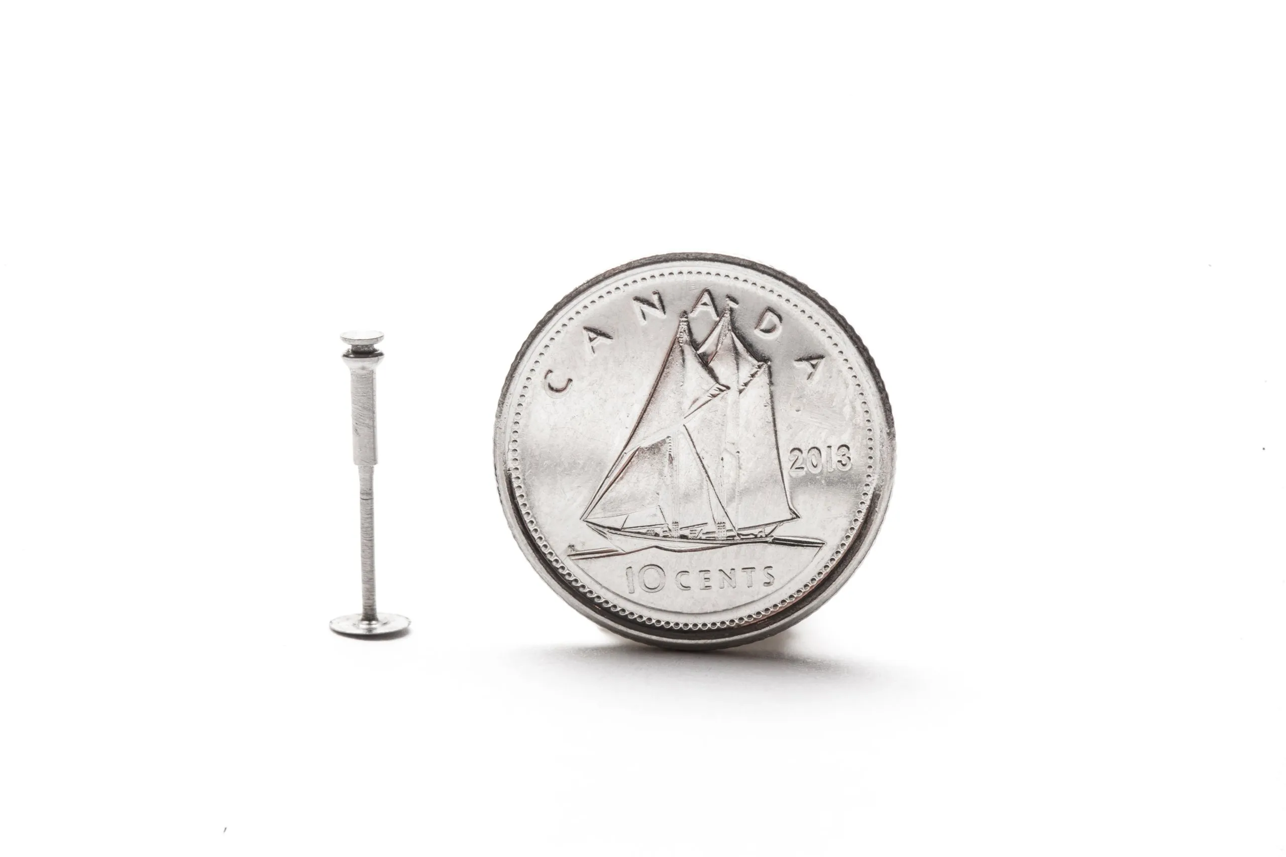 A tiny machined pin beside a Canadian ten-cent coin for scale