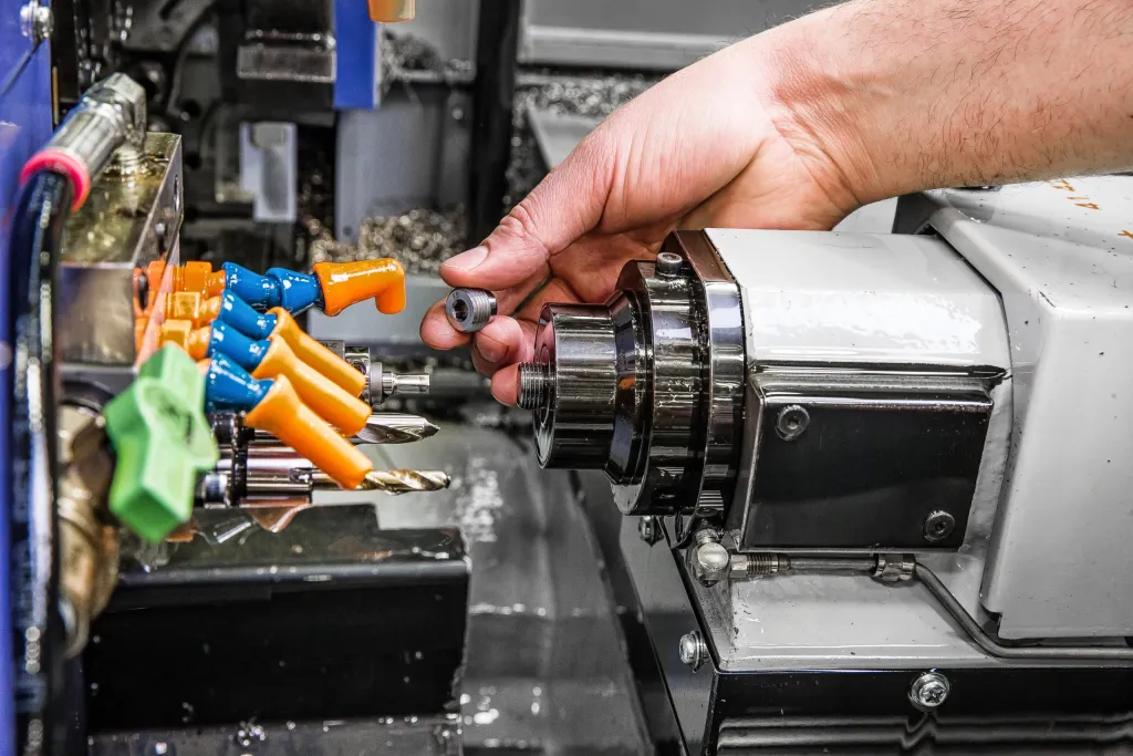 A hand reaching into a CNC lathe beside colourful coolant nozzles