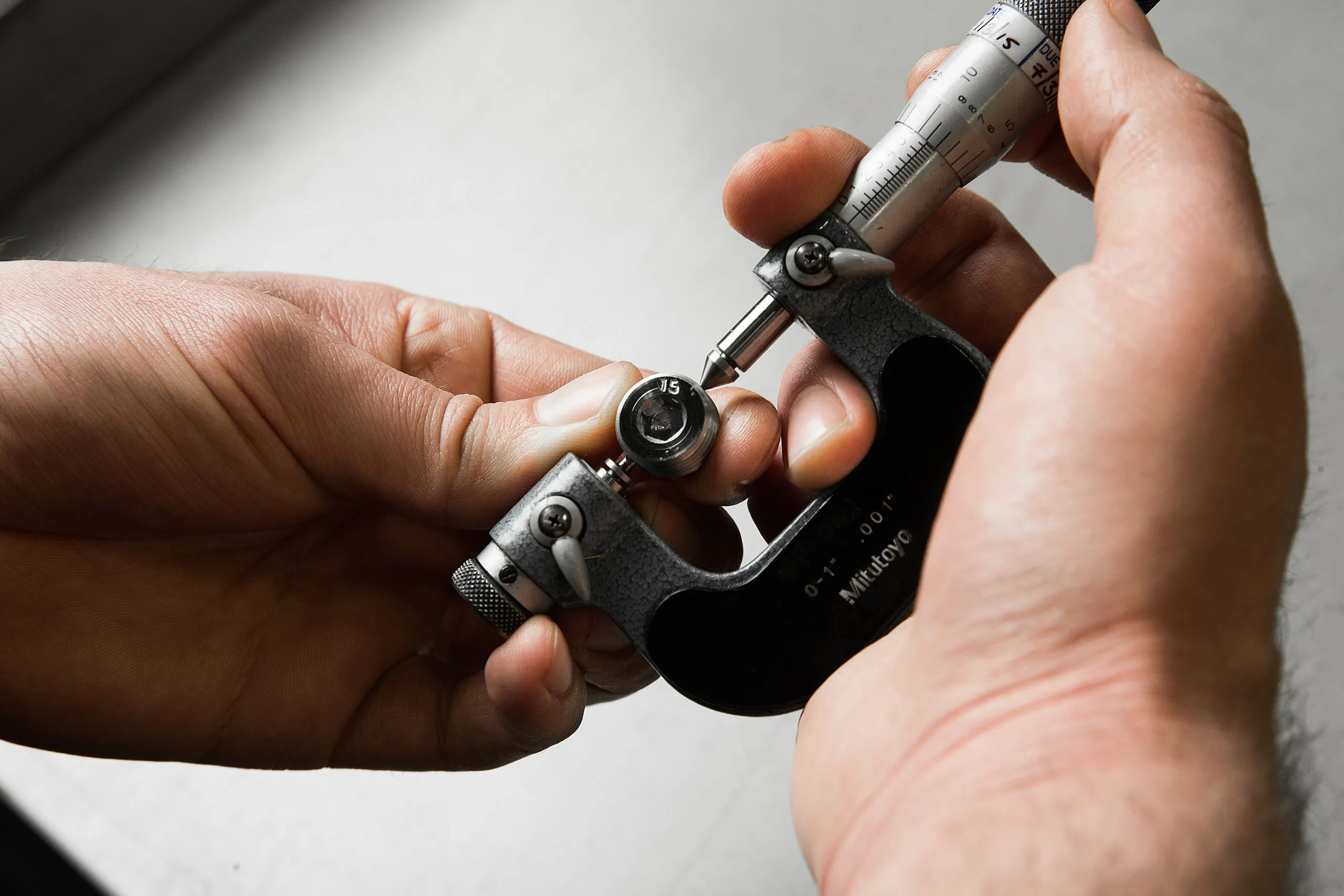 Hands checking a small machined part with a micrometer