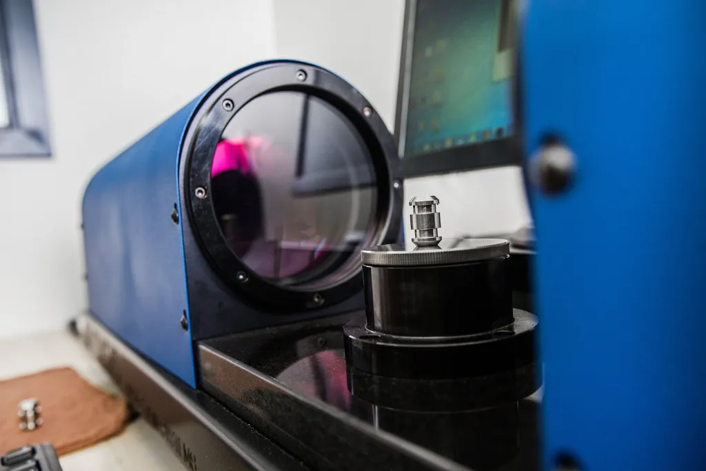 A small machined part on the stage of a blue measuring machine
